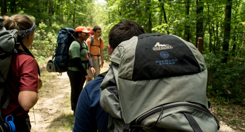 Backpackers hike along a trail through a wooded area